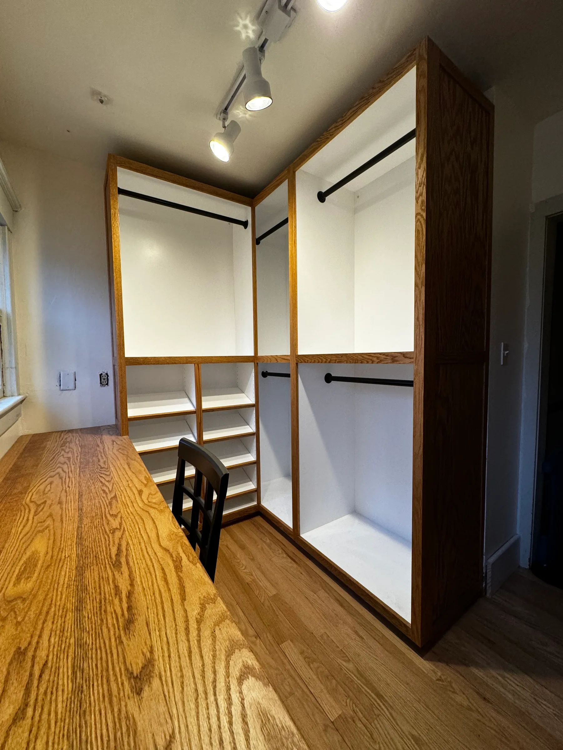 A fitted red oak walk-in closet with blackened steel hanging rods and open cubbies.